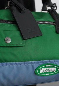 Green and blue nylon handbag with black leather accents, featuring a zip closure and logos, rectangular shape, and smooth texture.