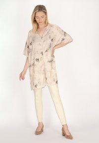 Lätt, beige kimono-topp med blommönster och korta ärmar, kombinerad med krämfärgade tajta byxor och beige klackar.