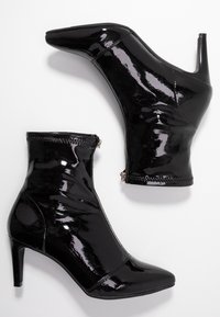 Par de botines negros brillantes con punteras afiladas, cremalleras laterales y tacones de altura media, sobre un fondo blanco.