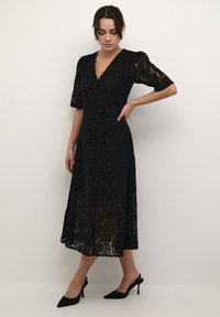 Black lace dress featuring a V-neck, short puff sleeves, and button detailing. The hem falls mid-calf, complementing pointed toe heels.
