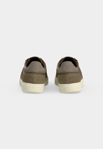 Paire de baskets en daim marron avec des colliers de talon rembourrés beiges et des semelles en caoutchouc blanches, vues de dos sur un fond uni.