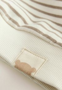 Tissu rayé présentant des couleurs beige doux et crème. Un carré avec un détail en silhouette d'ours est visible dans un coin.