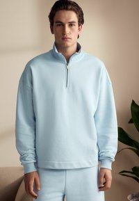 Sweatshirt din polar bleu deschis, cu guler cu jumătate de fermoar, Croială relaxată, manșete ribbate și textură netedă. Asortat cu pantaloni de trening corespunzători.