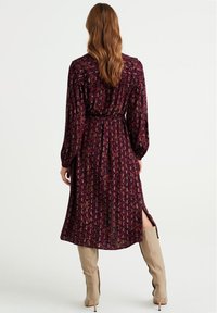 Lång, bordeauxfärgad klänning med blommönster; figursydd midja, veckdetaljer, långa ärmar och sidoklyftor. Kombinerad med beige knähöga stövlar.