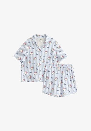 Pige står barfodet iført lyseblå, kortærmede pyjamas med knapper, dekoreret med Hello Kitty ansigter og sløjfer.