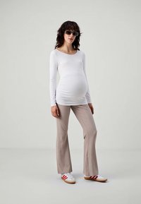 White long-sleeve top paired with light beige flared pants and white sneakers with red stripes. Model stands against a neutral background.