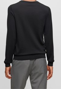 Černý lehký svetr s dlouhými rukávy, kulatým výstřihem, žebrovanými manžetami a pasem. Nosený s šedými texturovanými kalhotami.