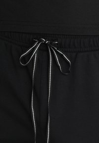 Shorts noirs avec une taille élastique, dotés d'un cordon de serrage noir et blanc et d'une texture lisse et douce. Design minimaliste sans motifs.