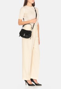 Borsa a mano nera con paillettes, dalla forma strutturata, con hardware in argento e tracolla regolabile, abbinata a pantaloni a vita alta crema a gamba larga e tacchi neri.