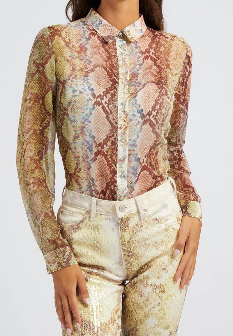 Chemise longue et transparente à manches longues avec un imprimé serpent multicolore. Elle comporte un col pointu et une fermeture par boutons. Associée à un pantalon métallisé orné de sequins.