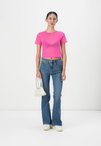 Top aderente a maniche corte e corto di un vivace rosa; abbinato a jeans in denim blu a zampa d'elefante e una piccola borsa bianca. Calzature: sneakers bianche.