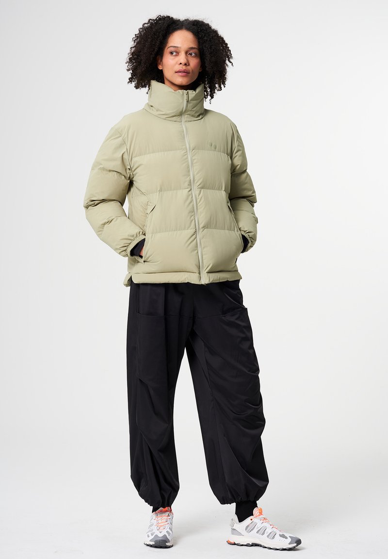 Puffige, hellgrüne Jacke mit hohem Kragen und Reißverschluss, kombiniert mit lockeren schwarzen Hosen und sportlichen weißen Sneakers.