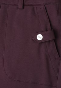 Gros plan sur un tissu violet foncé avec une poche munie d'un rabat et un bouton argenté gravé "Streetone Studio".