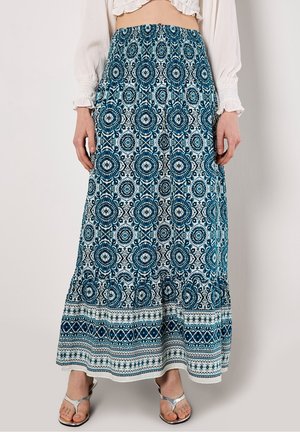 Jupe longue bleu et blanche à motifs floraux et géométriques portée avec un chemisier blanc et des sandales argentées.