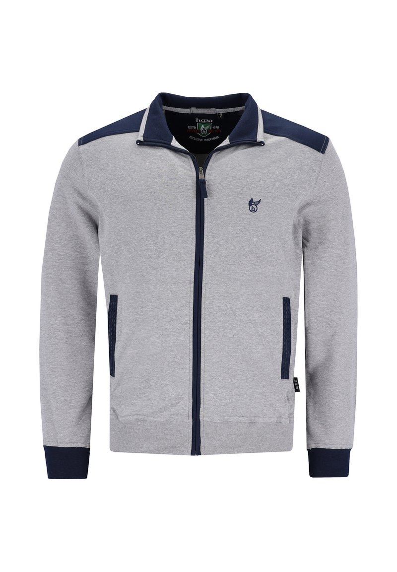 Grijze zip-up jas met marineblauwe accenten op de schouders en manchet, voorzien van een klein logo op de borst en zijzakken met ritssluiting. Zachte stoftextuur.