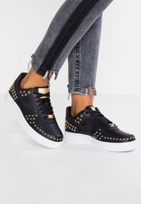 Sneakers nere con dettagli a stella dorata, texture liscia e suola bianca. Presentano una punta traforata e dettagli in metallo dorato.