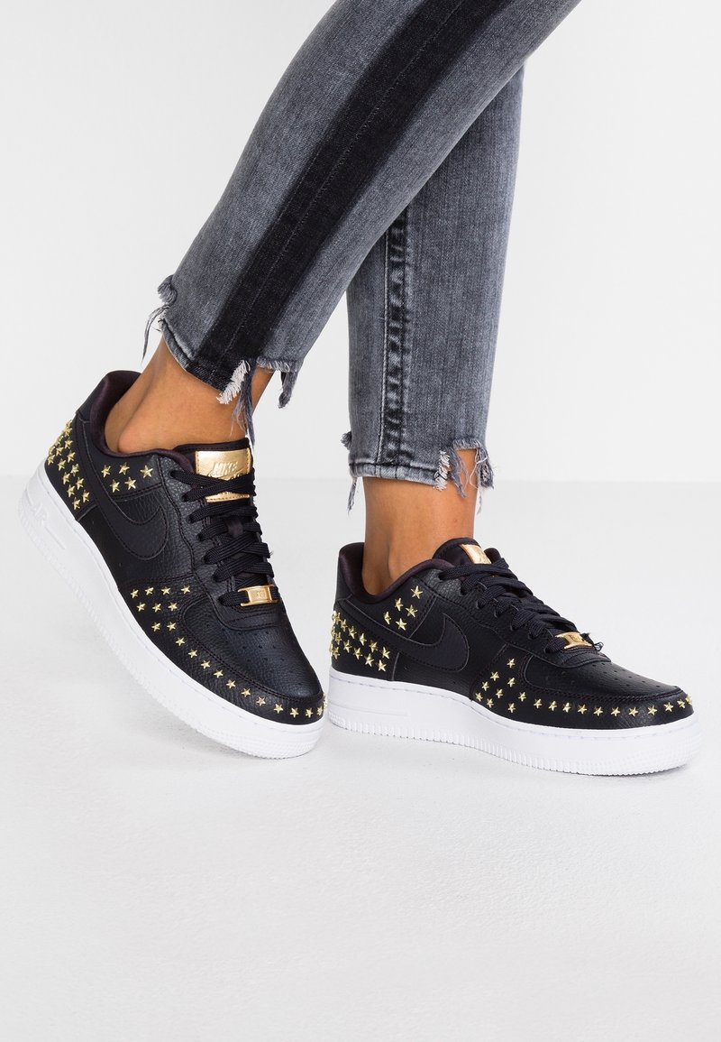 Sneakers nere con dettagli a stella dorata, texture liscia e suola bianca. Presentano una punta traforata e dettagli in metallo dorato.