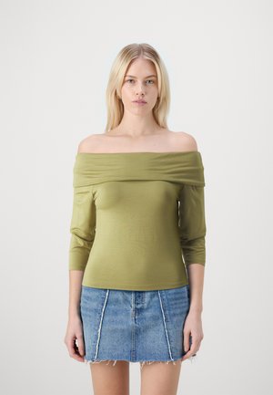 Olivno zeleni top brez naramnic s tremi četrtinami rokavov, gladka tekstura, prilega vegeti, v kombinaciji z raztrgano jeans mini krilom.
