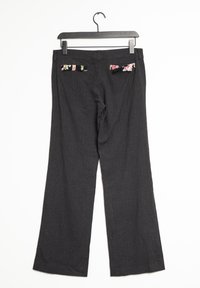 Pantalones de pierna ancha en tela oscura con sutiles rayas. Dos bolsillos traseros con acentos florales. Colgados de una percha de plástico negra.