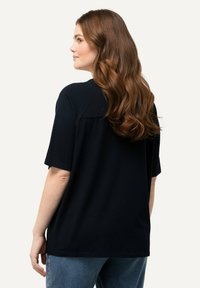 T-shirt nera a maniche corte con una vestibilità ampia, caratterizzata da un taglio dritto e un sottile dettaglio cucito sul retro, abbinata a jeans azzurri chiari.