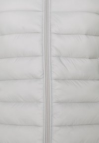 Polstret grå vest med glat, skinnende ydre, lodret quiltet mønster og en midterste lynlås med metalliske tænder.