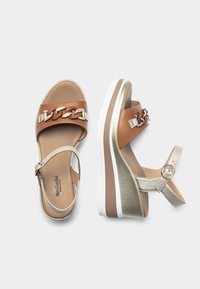 Brown leather platform sandals with a gold chain accent, metallic gold strap, and a white and brown sole. Adjustable ankle strap included.