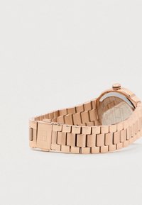 Rožu zelta metāla saitīšu pulksteņa aproce ar aizdari un apaļu pulksteņa aizmuguri, kas redzama uz gaiša fona.