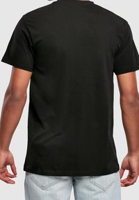 Schwarzes Baumwoll-T-Shirt, kurze Ärmel, Rundhalsausschnitt, lockere Passform, schlichte Rückansicht, getragen mit hellblauen Jeans. Keine Logos oder zusätzlichen Details.
