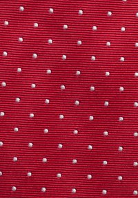 Röd tyg med ribbad textur har jämnt fördelade vita broderade prickar, vilket skapar en kontrast mellan färgerna och texturerna.