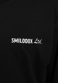 Camiseta de algodón negra con el logotipo en texto blanco "SMILODOX Ltd." en una fuente moderna en el frente. Textura suave, diseño de cuello redondo.