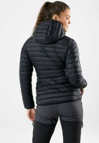 Black puffer jacket with horizontal quilted design, fitted hood, and elastic cuffs. Worn with gray pants featuring zippers and contrasting panels.