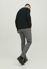 Zwarte geribbelde trui, grijze geruite broek en zwarte veterschoenen. De trui heeft een ronde hals en de broek heeft een slim fit.