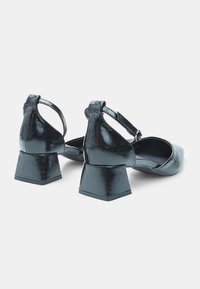 Black patent leather block-heeled shoes with ankle strap, squared toe, and a textured finish, featuring a slight sheen and a sturdy heel design.