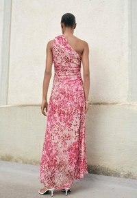 Maxikleid mit einem Schulterträger aus hellpinkem Stoff mit roten und dunkelpinkfarbenen Spritzmustern; verfügt über ein tailliertes Oberteil und einen fließenden Rock.