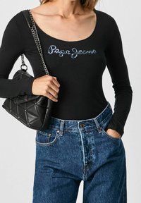 Schwarzer Langarm-Bodysuit mit glitzerndem "Paco Jeans"-Logo, kombiniert mit hochgeschnittenen blauen Denim-Jeans und einer schwarzen gesteppten Handtasche.