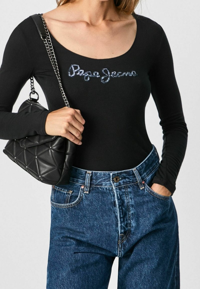 Schwarzer Langarm-Bodysuit mit glitzerndem "Paco Jeans"-Logo, kombiniert mit hochgeschnittenen blauen Denim-Jeans und einer schwarzen gesteppten Handtasche.