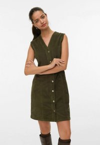 Olivijnkleurige corduroy jurk met een V-hals, mouwloos ontwerp, knoopjes aan de voorkant en twee zijzakken. Glad, textuur oppervlak.
