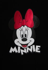 Camiseta gráfica de Minnie Mouse que presenta a un personaje en blanco y negro con un gran lazo rojo y el nombre "MINNIE" en letras blancas en negrita.