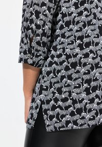 Sort bluse med gentaget hvidt zebra print, med trekvartlange ærmer og slids i siden, lavet af et blødt, glat stof.