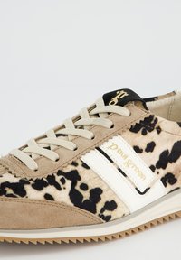 Baskets beige à pois noirs en suède et tissu, avec des lacets crème, des bandes blanches et une languette noire ornée d'un logo doré.