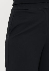 Svarte sporty bukser laget av myk, elastisk stoff. Har elastisk midjebånd og side lommer for bekvemmelighet.