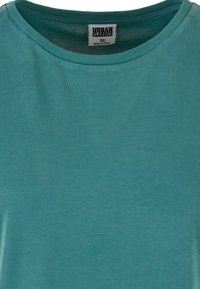 T-shirt col rond bleu sarcelle avec étiquette "Urban Classics" cousue à l'intérieur du col, taille XS, fabriqué en Chine.