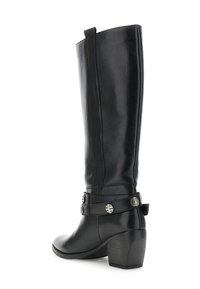 Bota de cuero negra hasta la rodilla con tacón cuadrado y correa decorativa con tachuelas plateadas alrededor del tobillo.