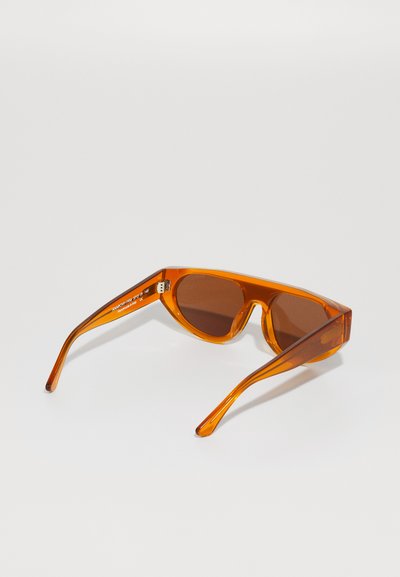 Orange sunglasses with a sleek, angular design, featuring brown lenses and thin, transparent temples. No visible branding or patterns.