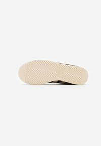 Sneaker marrone con suola in gomma texture, caratterizzata da un motivo a spina di pesce. La suola presenta un logo prominente e bordi lisci.