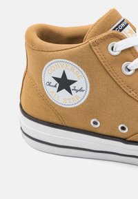 Hnědé plátěné vysoké tenisky s bílou gumovou podrážkou, černým pruhem a ikonickou hvězdnou nášivkou s textem "Converse" a "Chuck Taylor".