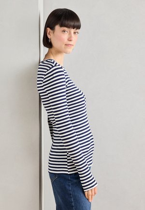 Haut à rayures bleu marine et blanches à manches longues avec un design ajusté, texture côtelée, encolure ronde et fentes latérales, associé à un jean bleu.