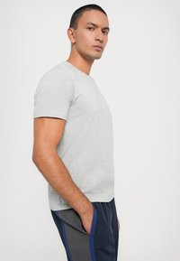 Pelēka īsām piedurknēm T-kreklu ar apaļu kakla izgriezumu, gluda tekstūra un pieguļoša forma, apvienots ar tumšiem biksēm ar kontrastējošām zilo akcentiem.