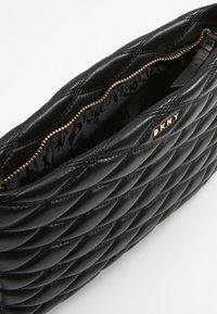 Clutch DKNY in pelle trapuntata nera con zip dorata, parzialmente aperto che mostra la fodera interna in tessuto brandizzato.