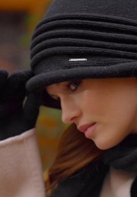 Cappello di lana nera con design plissettato e un accento argentato. La texture appare morbida e calda, adatta per il clima più fresco.